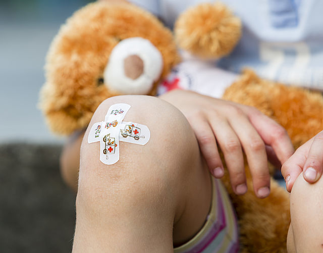 Knie eines Kindes mit Pflaster, Das Kind hält einen Teddybären