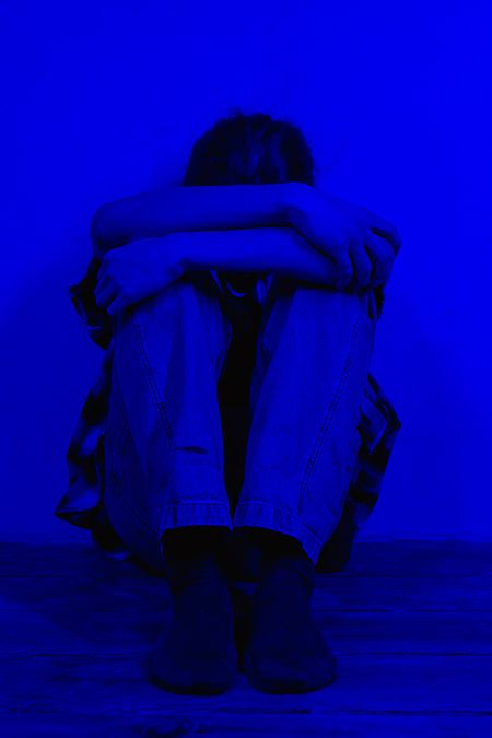 Erste Hilfe für die Psyche Person sitzt zusammengekauert in der Ecke, blau gefärbt