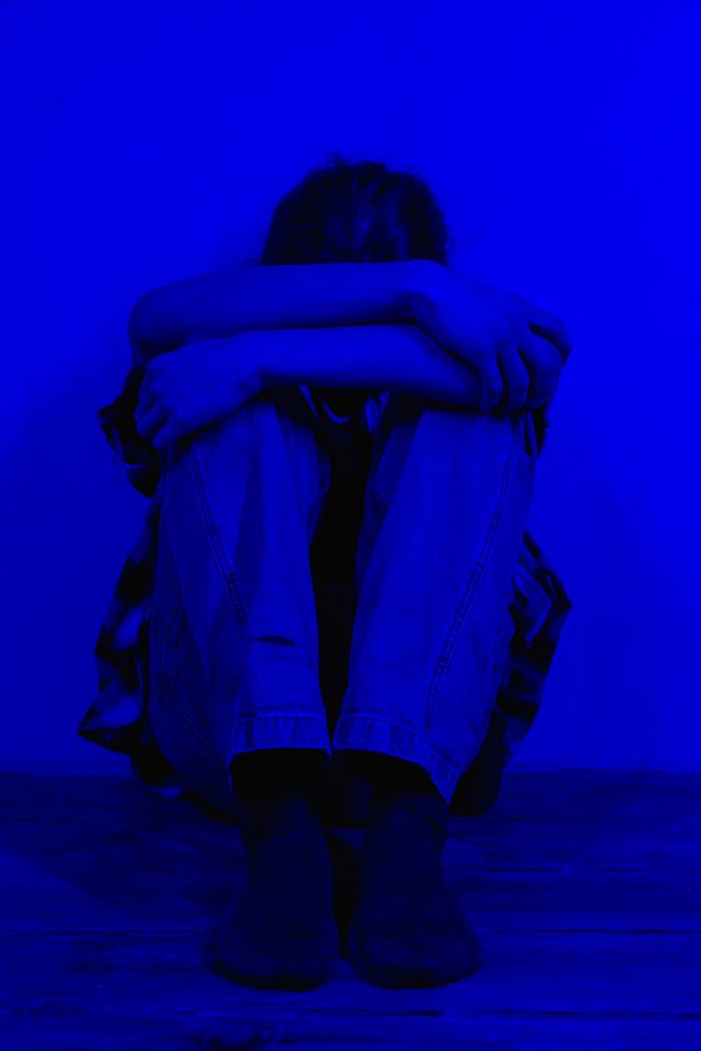 Person sitzt zusammengekauert in der Ecke, blau gefärbt